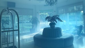 Un hall amplio con una lámpara moderna, ventanas grandes y una zona de estar central con una planta en maceta.