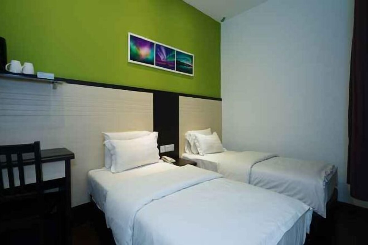A hotel room with two beds, a desk, and a green accent wall.