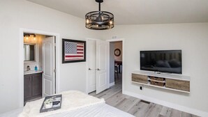 Ein Schlafzimmer mit Bett, Fernseher, einer Chandelieber und einer Tür zum Badezimmer.