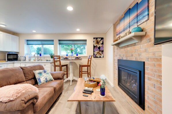 A modern kitchen with white cabinets, a dining area with a table and chairs, a fireplace, and a large window with a view of trees. - 2 Mi to St Edward State Park: Ground-Level Studio (Kenmore)