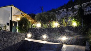 Une vue nocturne d’un bâtiment doté d’un mur en pierre, d’un escalier menant à une porte et de plusieurs sources de lumière.