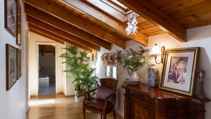 Une pièce avec des poutres en bois, une chaise, un bureau, un vase de fleurs et un tableau encadré.