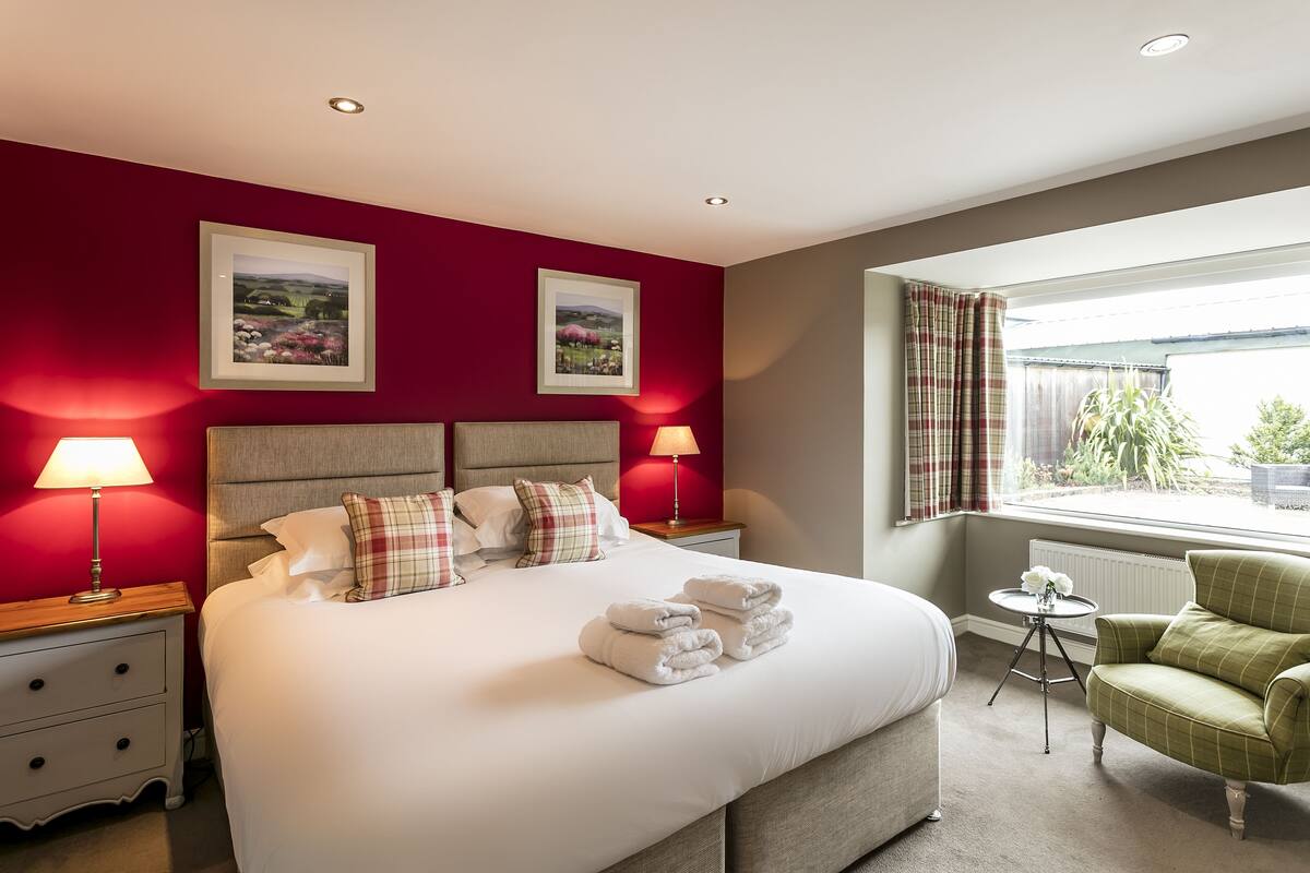 A hotel room with a large bed, two bedside lamps, a green armchair, and a window with curtains.