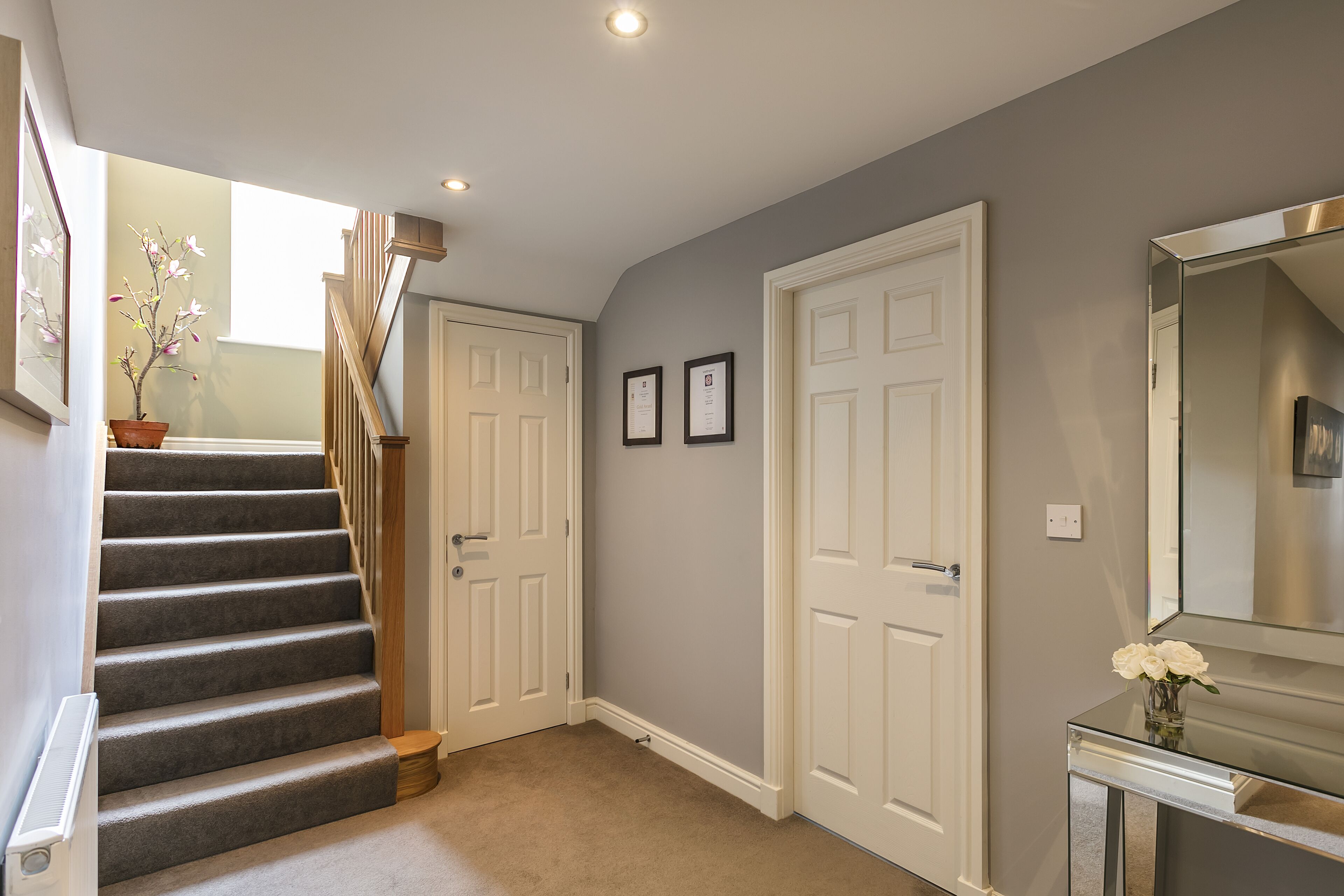 A hallway with a carpeted staircase, white doors, and a mirror on a console table.