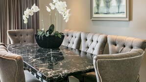 Un coin repas avec une table en marbre, des chaises rembourrées et un vase rempli de fleurs blanches.
