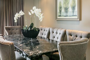 A dining area with a marble table, upholstered chairs, and a vase of white flowers.