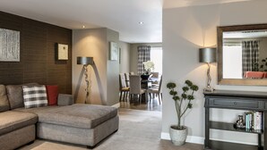 Un salon moderne avec un canapé d’angle, un coin repas comprenant une table et des chaises, un grand miroir et une plante en pot.