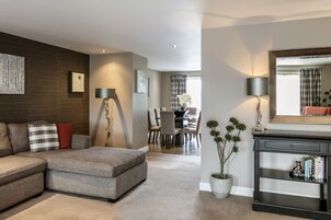 A modern living room with a sectional sofa, a dining area with a table and chairs, a large mirror, and a potted plant.