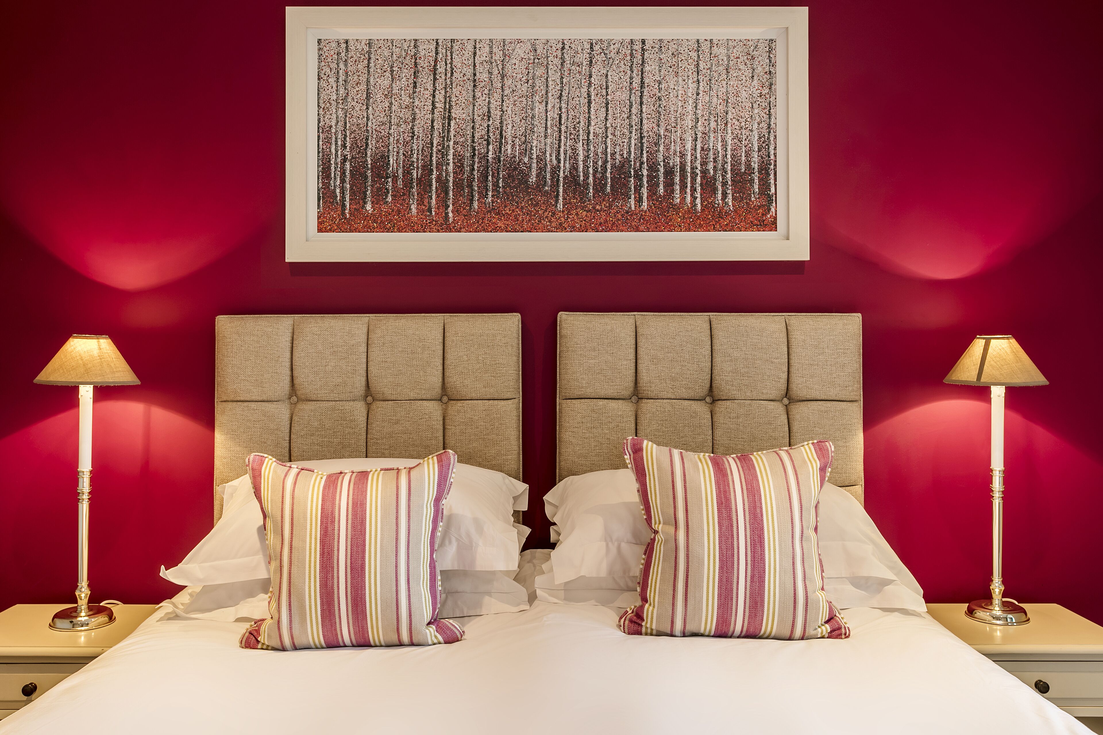 A double bed with striped pillows, a tufted headboard, and a framed artwork above.