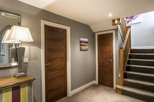 A hallway with two wooden doors, a lamp, and a painting on the wall.