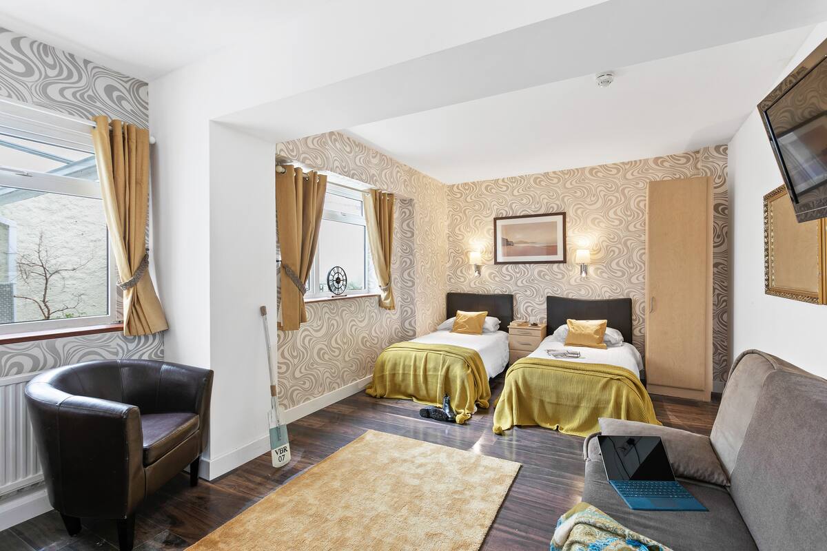 A hotel room with two beds, a sofa, a chair, a laptop, and a window with curtains.