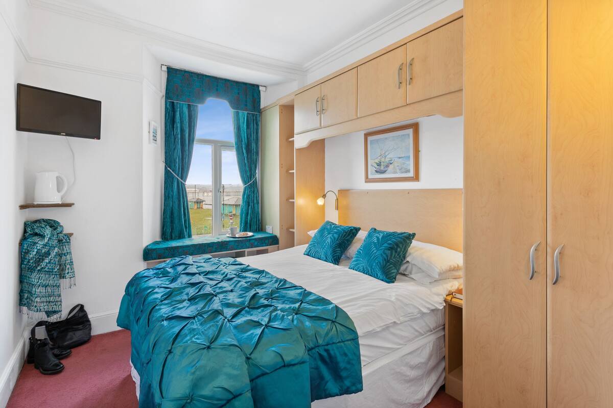 A hotel room with a bed, a window with curtains, a television, and a wardrobe.