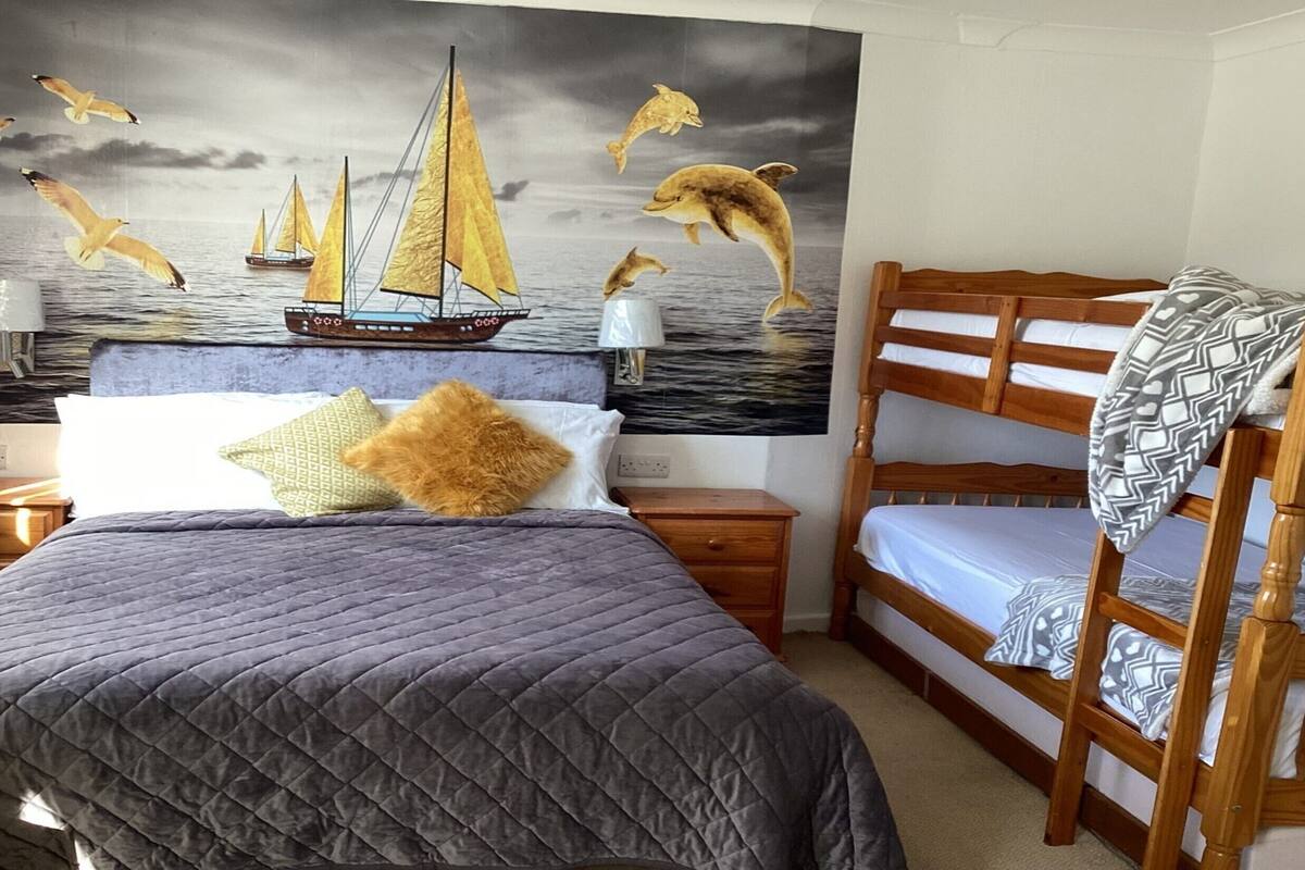 A bedroom with a bed, a nightstand, a wooden bench, and a mural of sailboats and dolphins.
