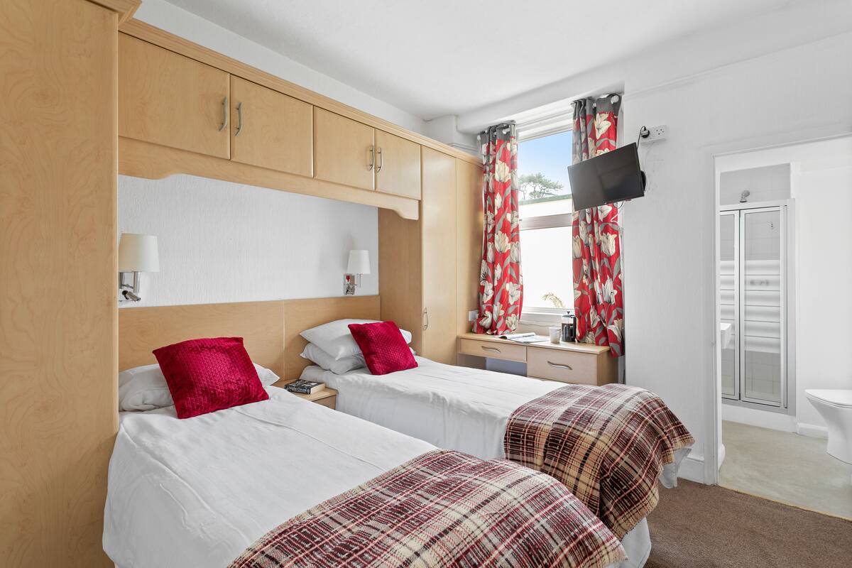 A hotel room with two beds, wooden wardrobe, a TV, and a bathroom with a toilet and shower.