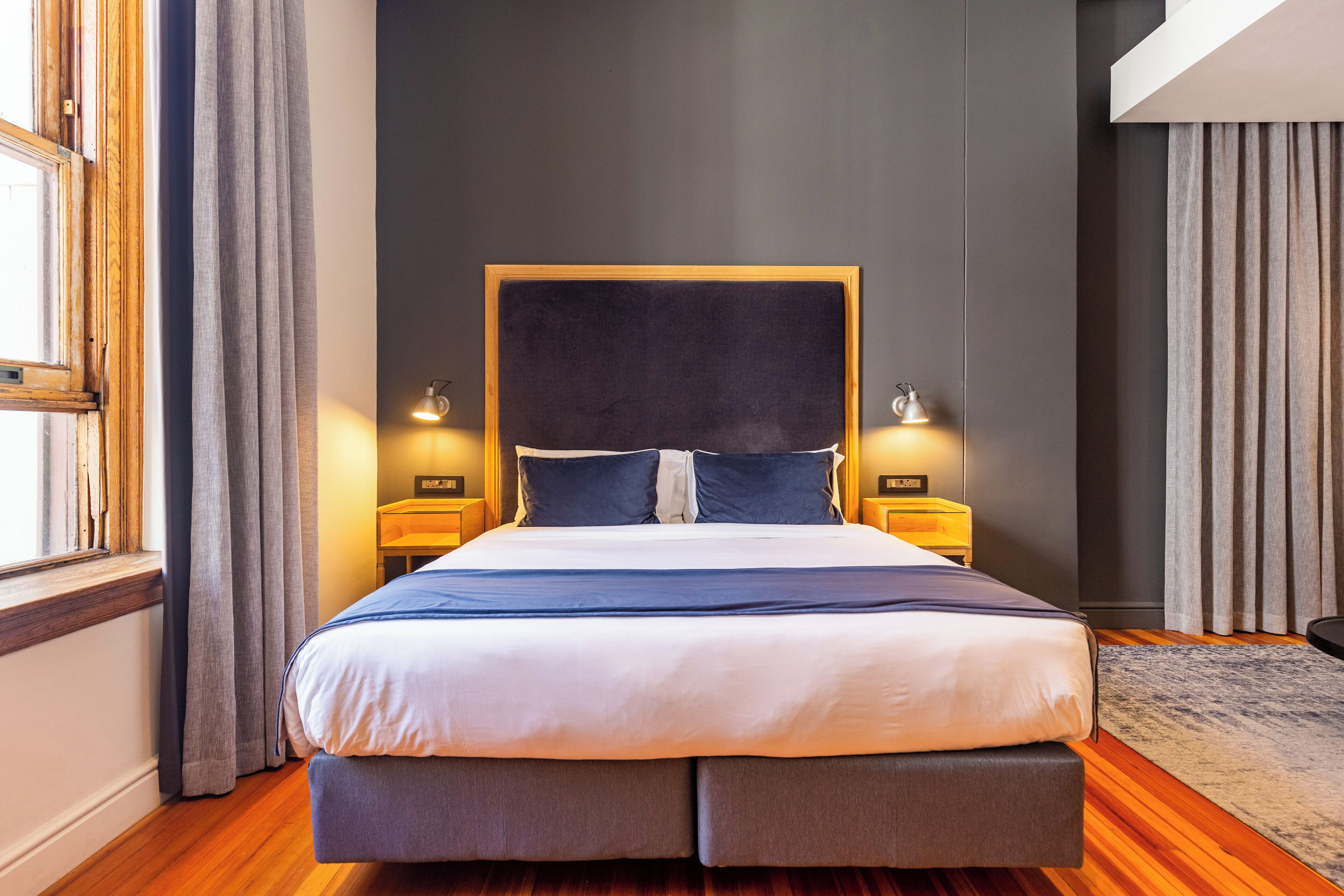 A modern bedroom with a large bed, wooden headboard, and two bedside lamps.