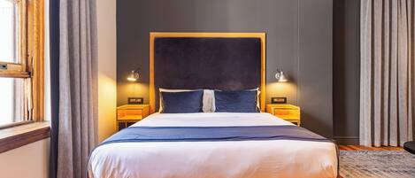 A modern bedroom with a large bed, wooden headboard, and two bedside lamps.