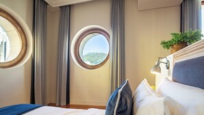 A hotel room with a large bed, a round window, a potted plant, and a lamp. - Old Bank Hotel (Cape Town)