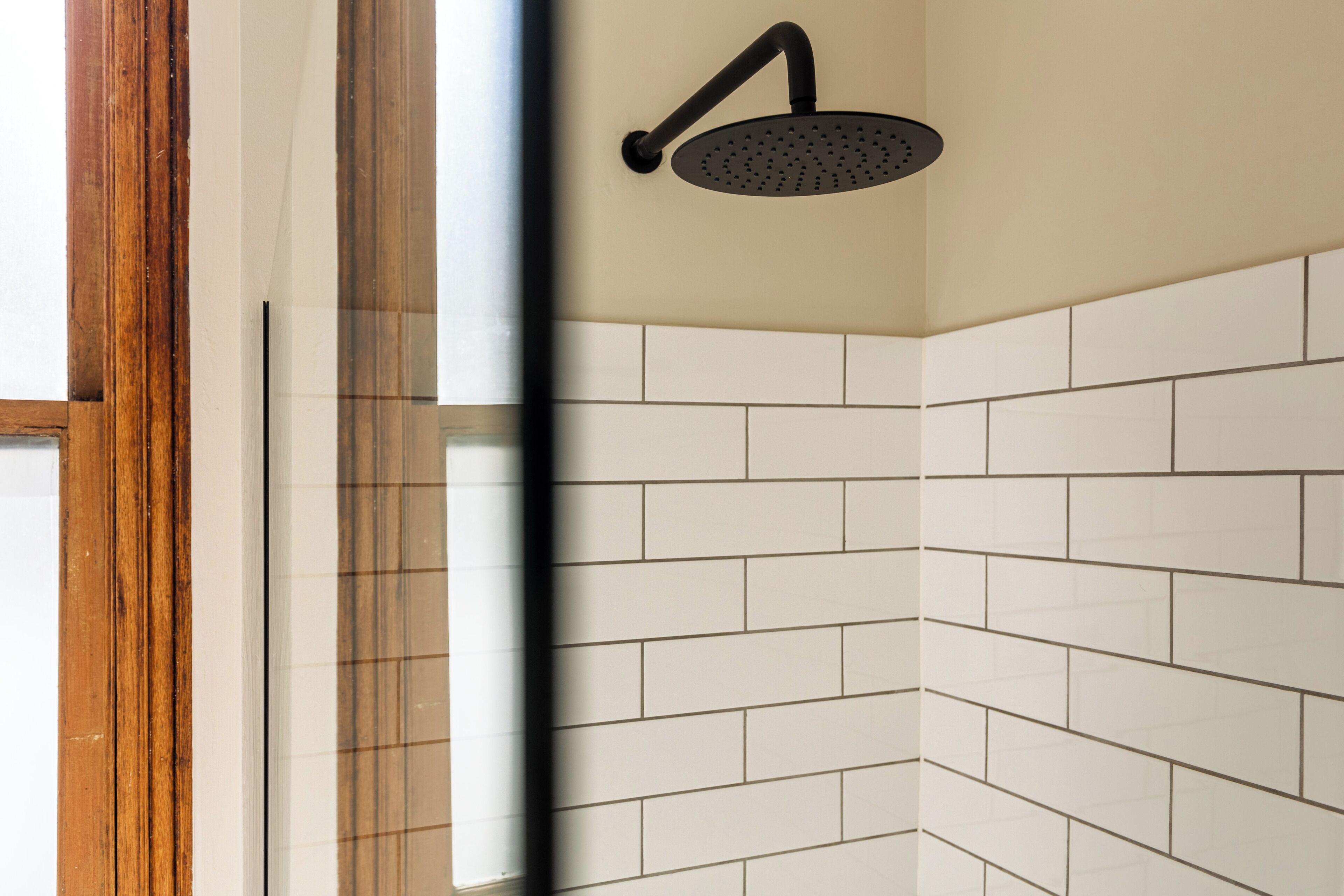 Rincón de un baño con azulejos blancos tipo metro y una ducha con cabezal negro.