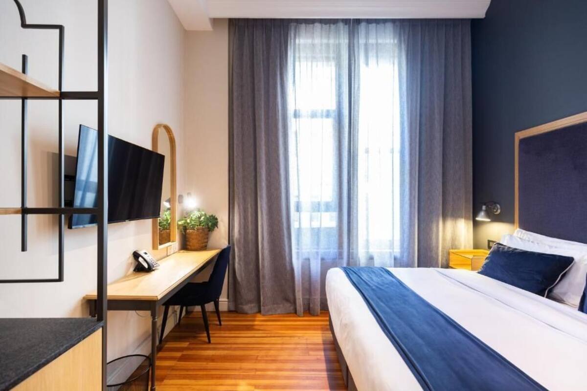 A hotel room with a bed, desk, chair, television, and curtains.