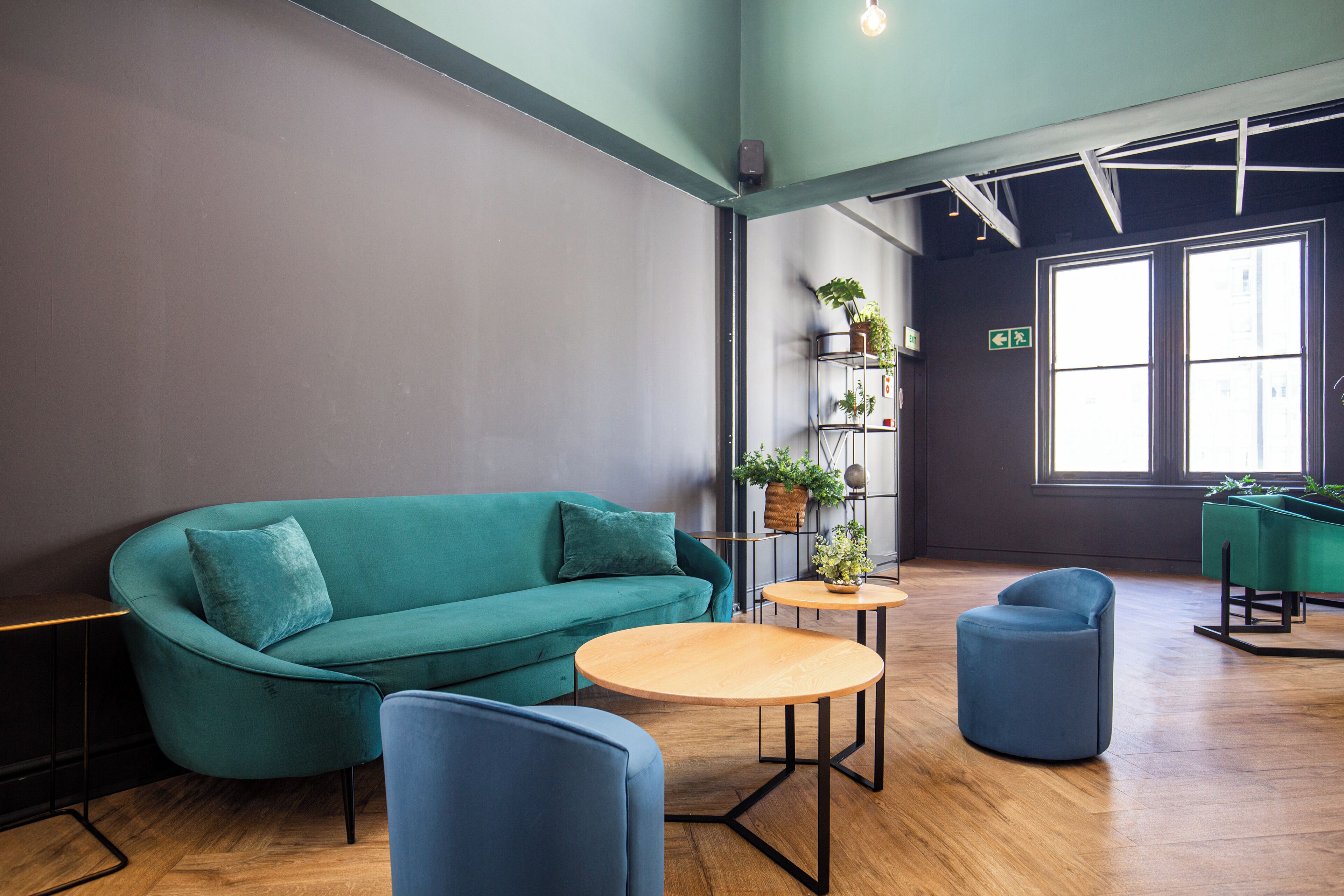 A modern lounge area with a teal sofa, round wooden tables, and blue chairs.