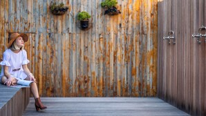 A person sitting on a wooden ledge in front of a rustic wooden wall with potted plants. - Old Bank Hotel (Cape Town)