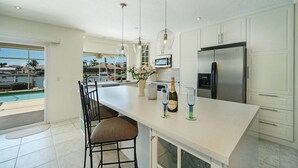 Una cocina moderna con una isla grande, muebles blancos, electrodomésticos de acero inoxidable y vista a una piscina.