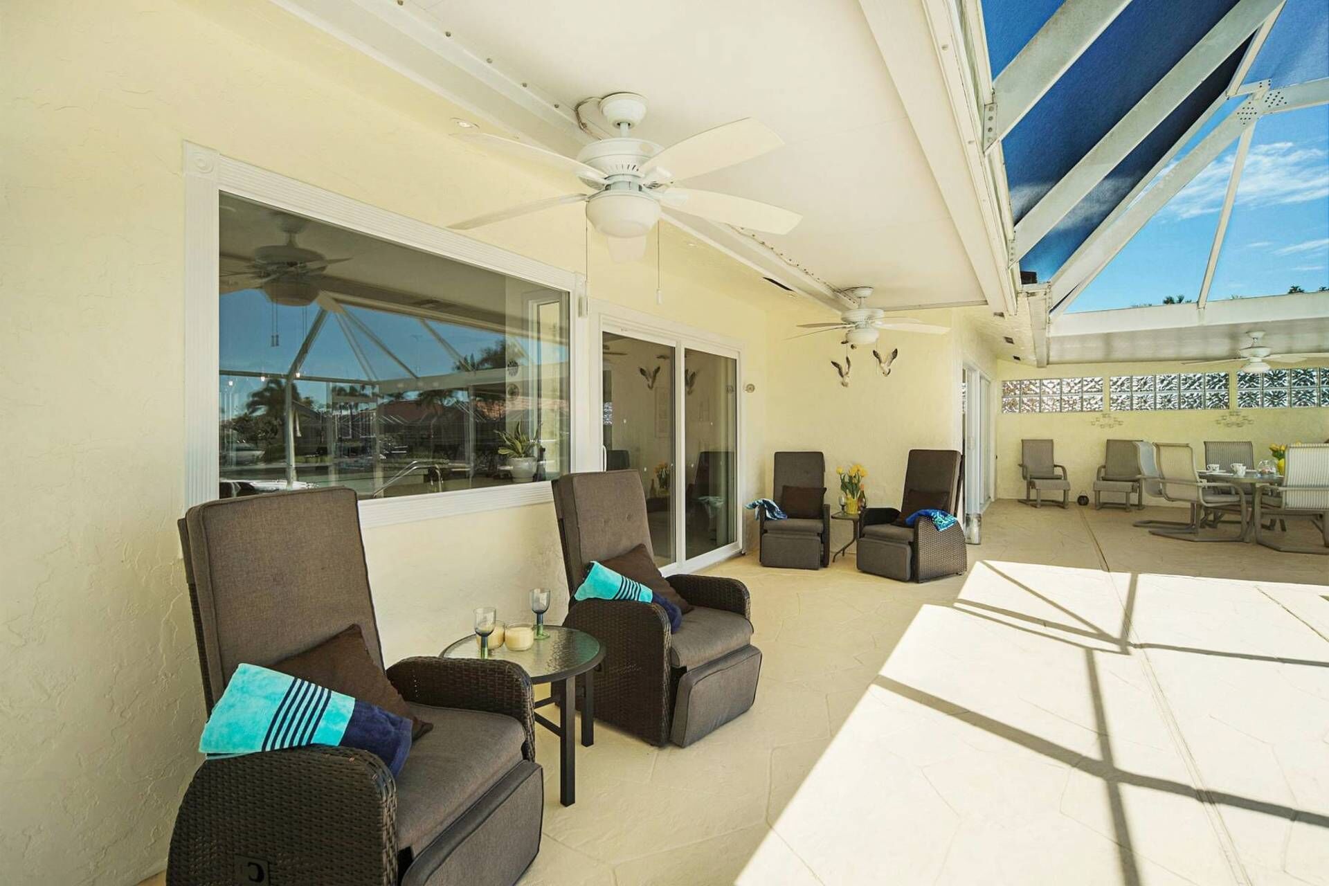 A sunlit patio with wicker furniture, a ceiling fan, and a view of the pool area.