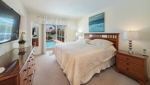 Un dormitorio con una cama grande, televisión, escritorio y vistas a una piscina y al océano.