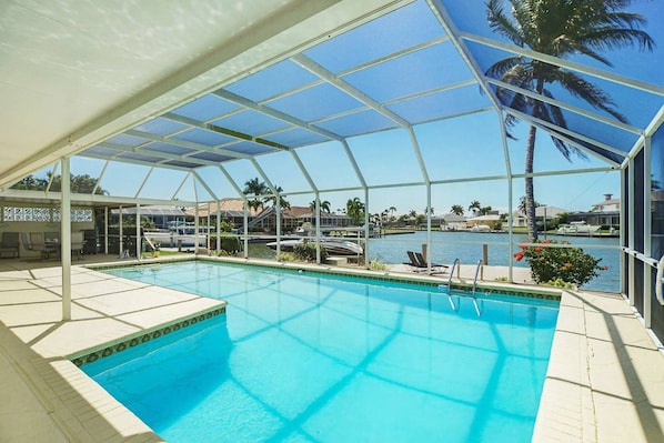 A pool area with a clear view of the water, a covered seating area, and a view of the marina with boats.