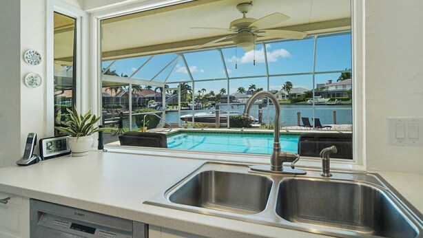 Una cocina con un amplio ventanal que da a una zona de piscina, un ventilador de techo y un lavavajillas Bosch.