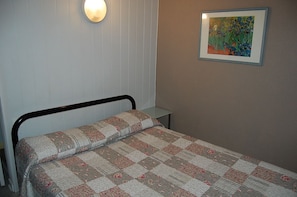 A single bed with a floral quilt, a bedside table, a wall-mounted light, and a framed painting of flowers. - Hôtel des Jacobines (Chalon-sur-Saone)