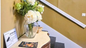 A staircase with a painting on the wall, a vase with flowers, and a sign with a camera icon. - Hôtel des Jacobines (Chalon-sur-Saone)