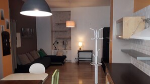 A modern living room with a sofa, a dining table, and a kitchen area with a microwave. - Hôtel des Jacobines (Chalon-sur-Saone)
