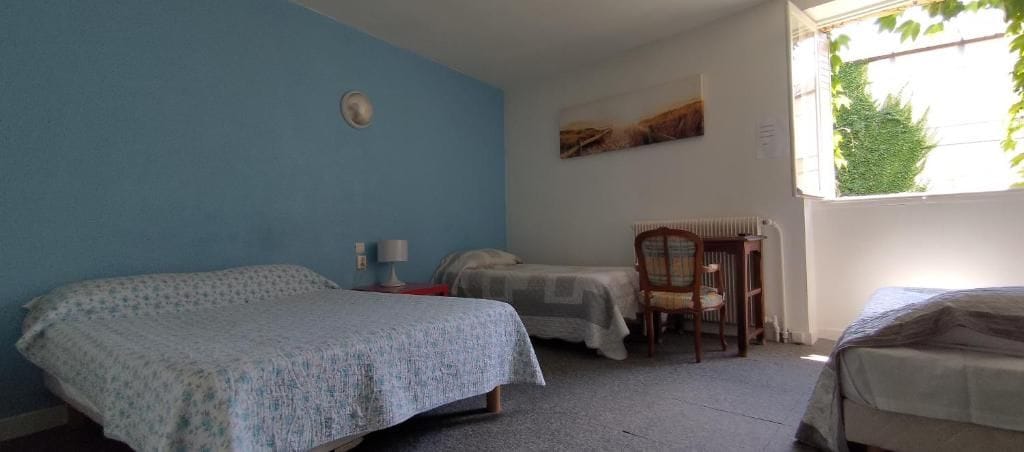 A room with two beds, a chair, a table, and a window.