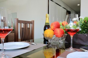 A dining table with a bottle of champagne, a bowl of fruit, and two glasses of red wine. - The Art - Xuan Hoa Hotel & Apartments (Hanoi)