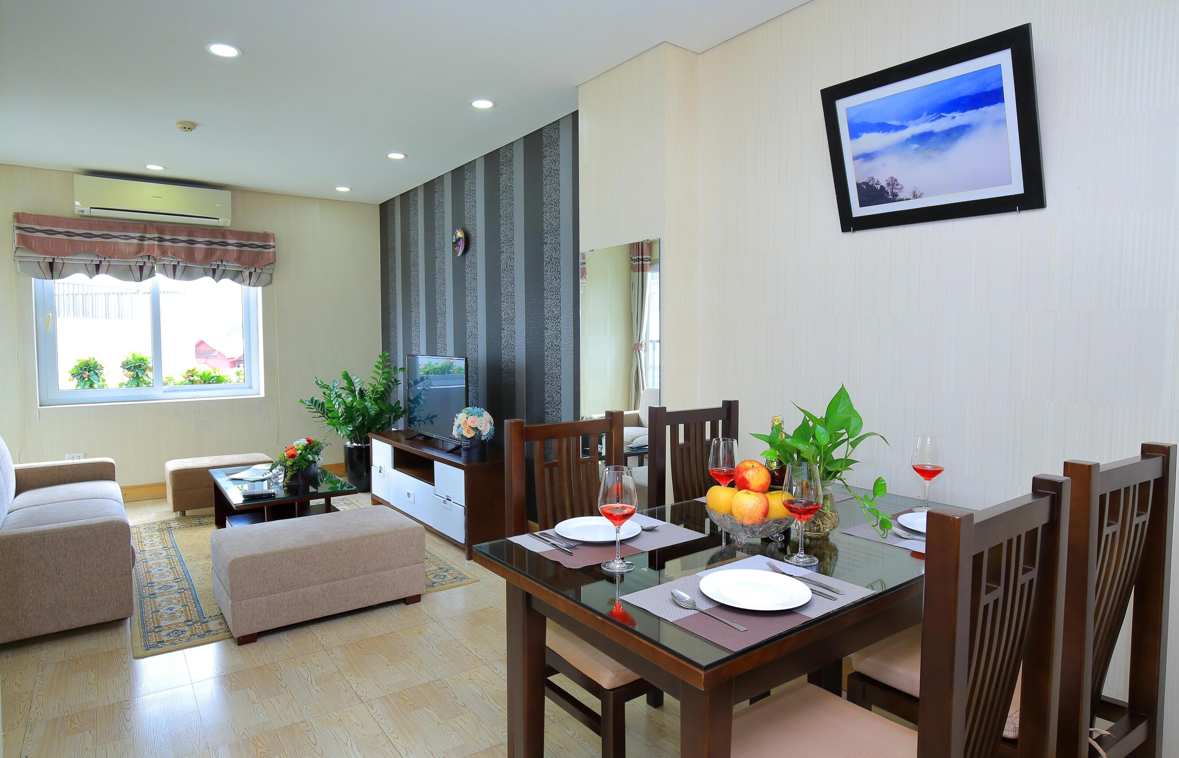 A dining area with a glass table, wooden chairs, and a TV in the background.
