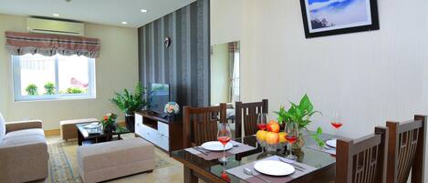 A dining area with a glass table, wooden chairs, and a TV in the background.