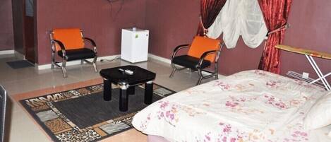 A hotel room with a bed, two chairs, a small table, a TV, and a refrigerator.