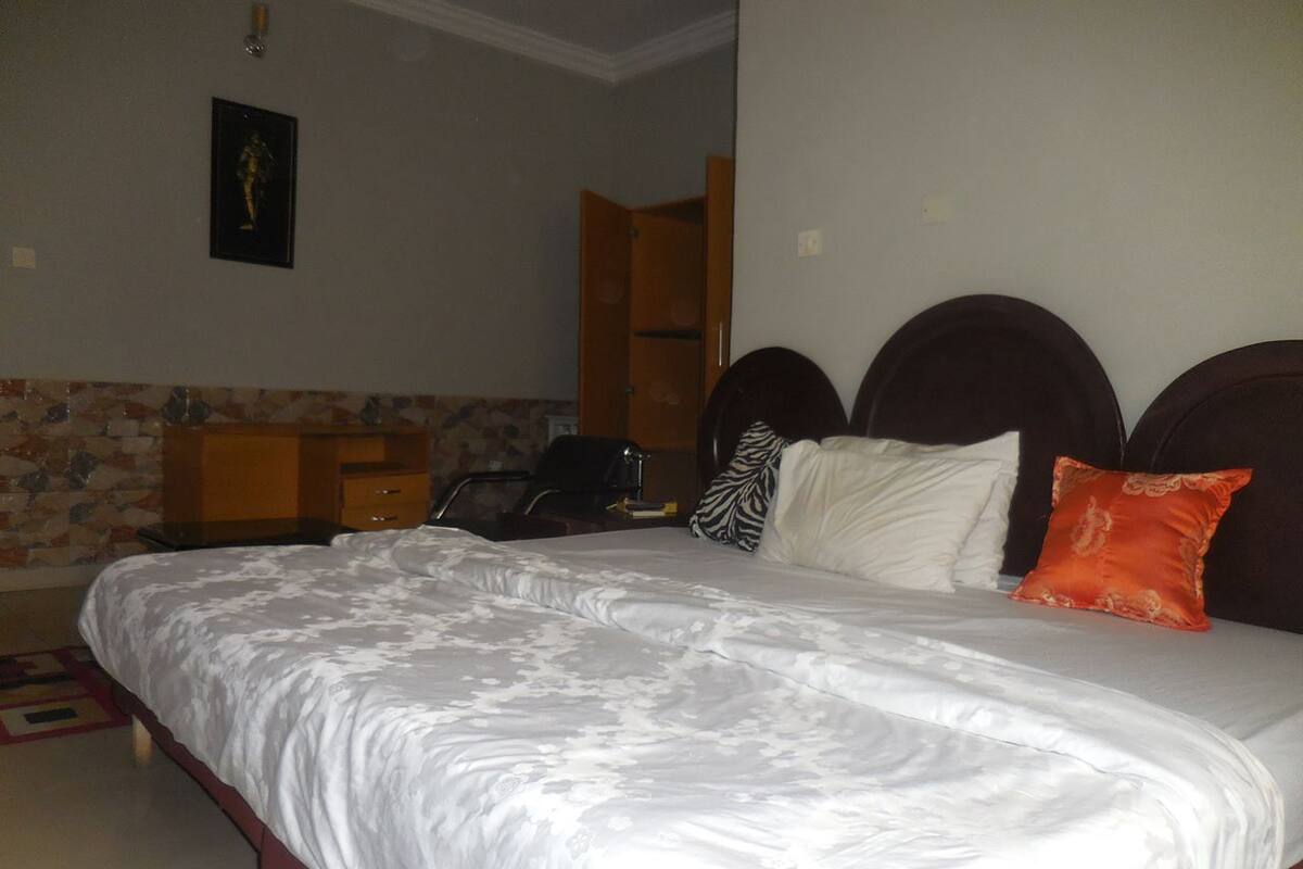 Une chambre à coucher avec un lit, des oreillers, une table de chevet, une commode et un tableau accroché au mur.