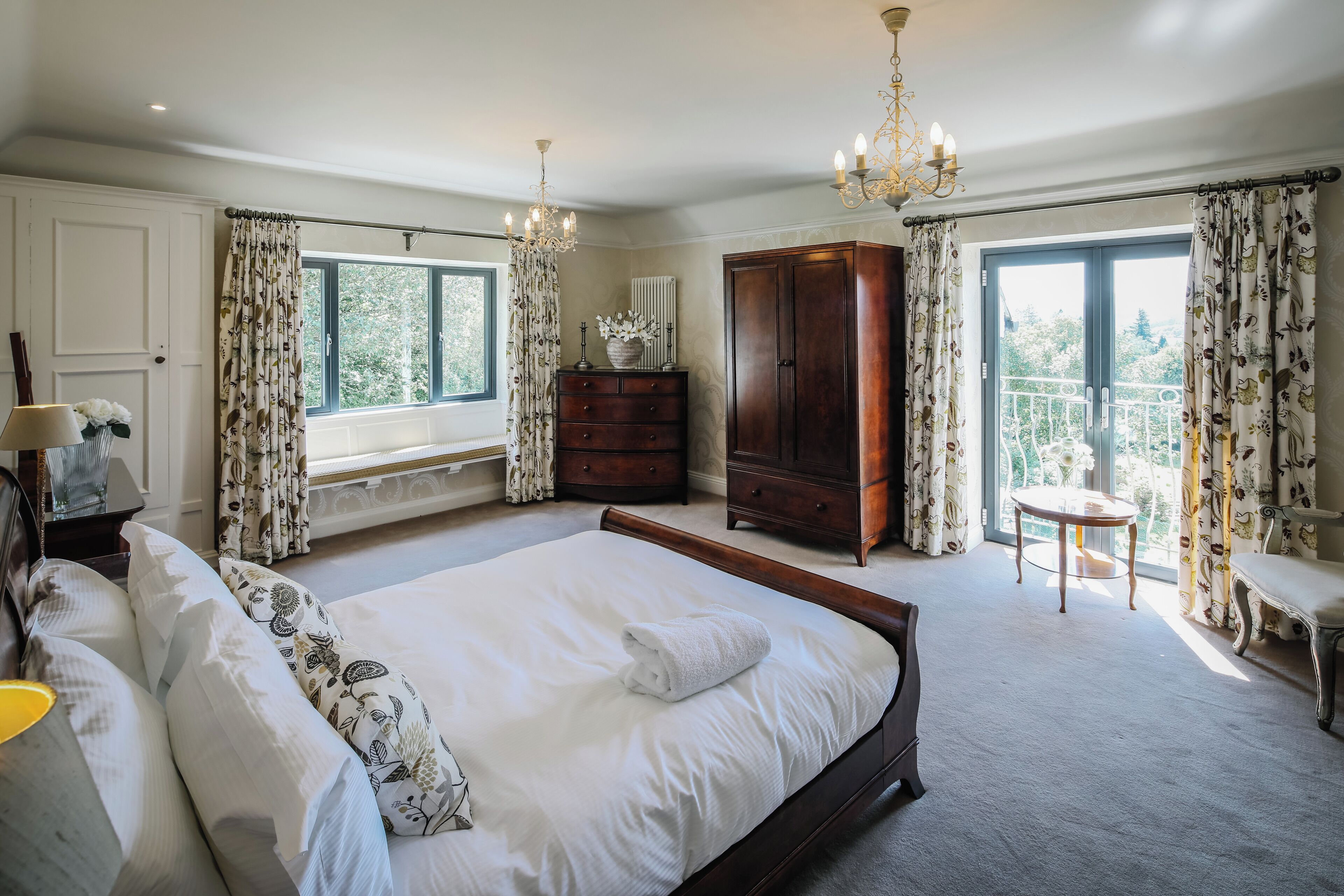 A spacious bedroom with a large bed, a dresser, and a balcony with a table.