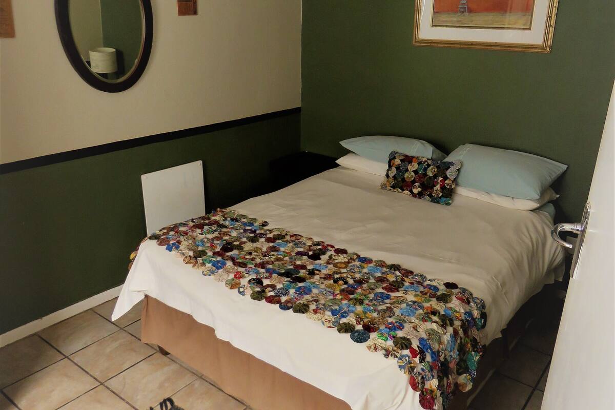 A bedroom with a bed, pillows, a mirror, and a framed picture on the wall.