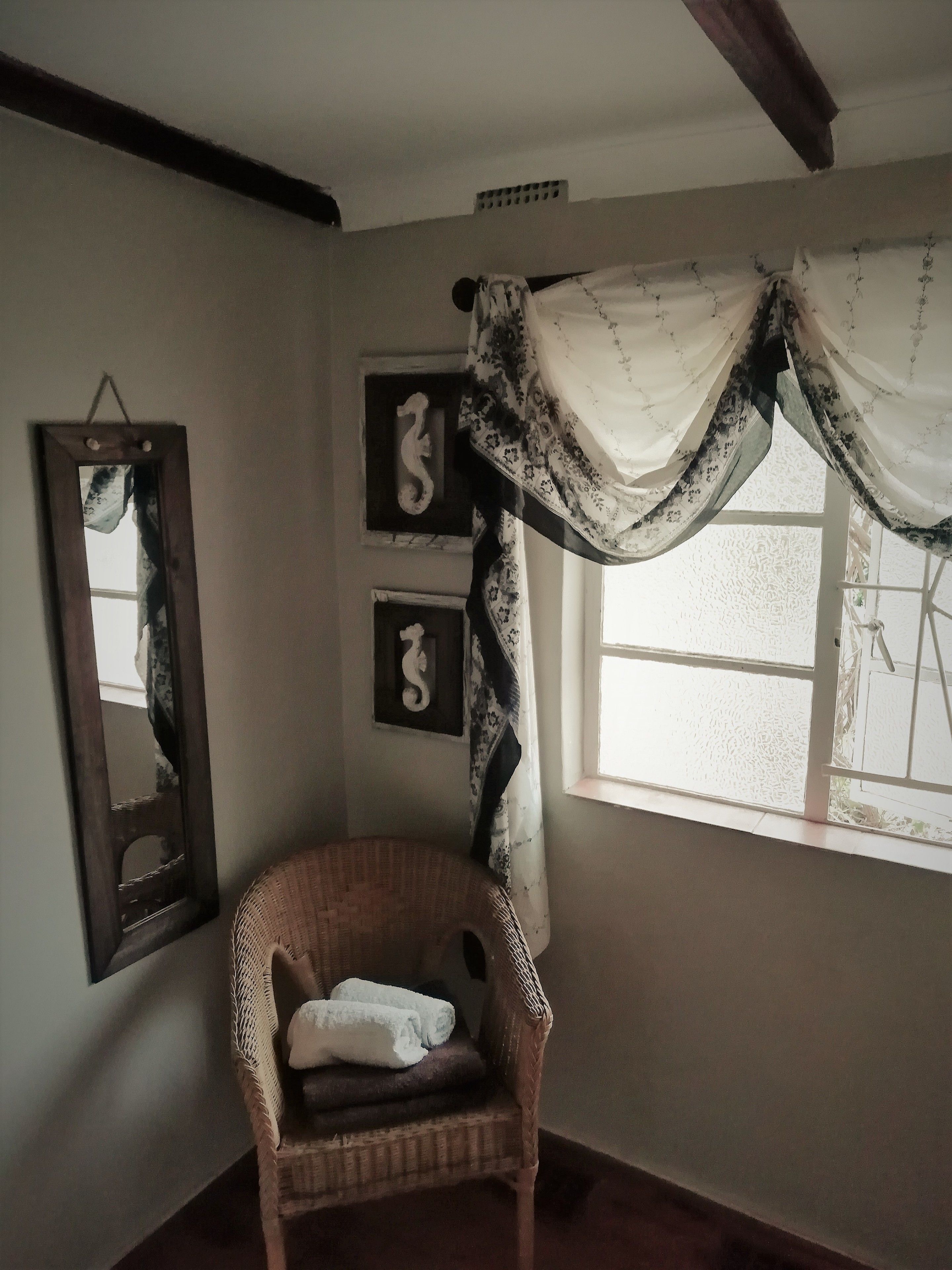A room with a wicker chair, a mirror, and a window with a sheer curtain.