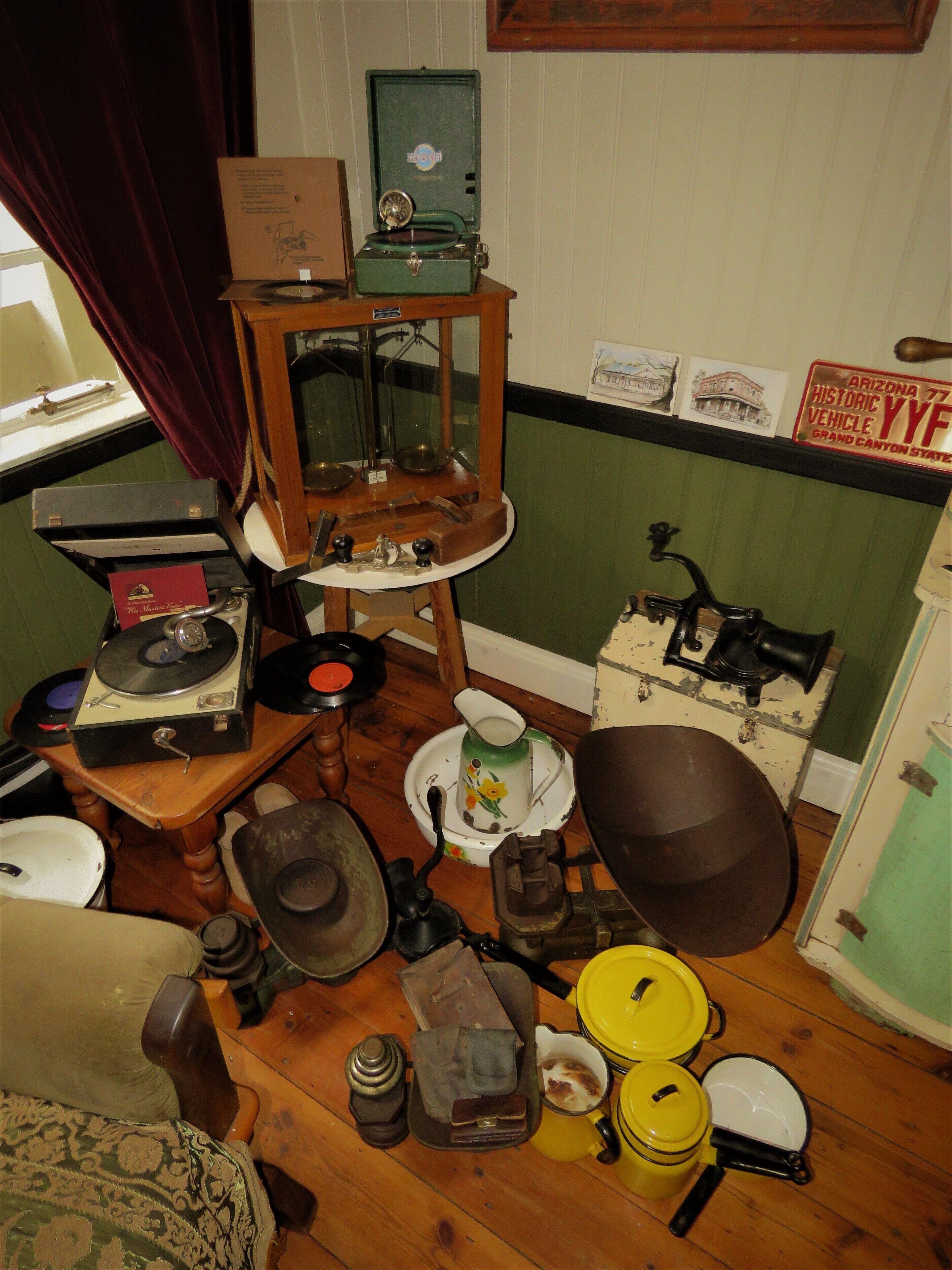 Une pièce encombrée, où se trouvent divers objets anciens, notamment un gramophone, une radio d’époque et de vieux ustensiles de cuisine.