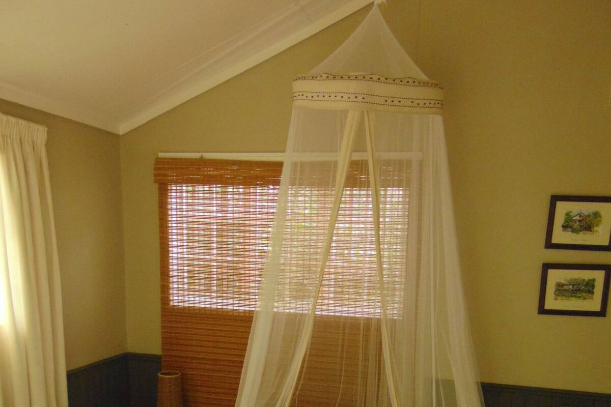 A bed with a canopy, a window with blinds, and a wall with framed pictures.