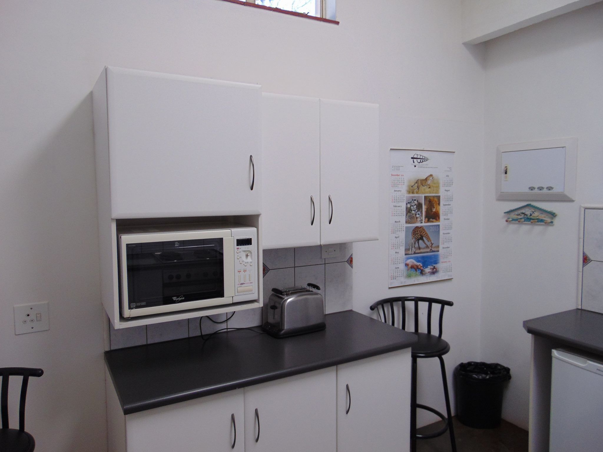 Eine kompakte Küche mit weißen Schränken, einer Mikrowelle, einem Toaster und einem Kalender an der Wand.