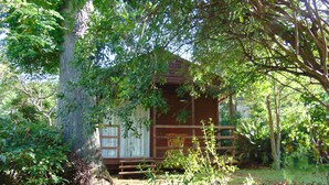 A rustic cabin with a wooden exterior, surrounded by lush greenery and flowering plants. - Fountain Baths Guest Cottages (Barberton)