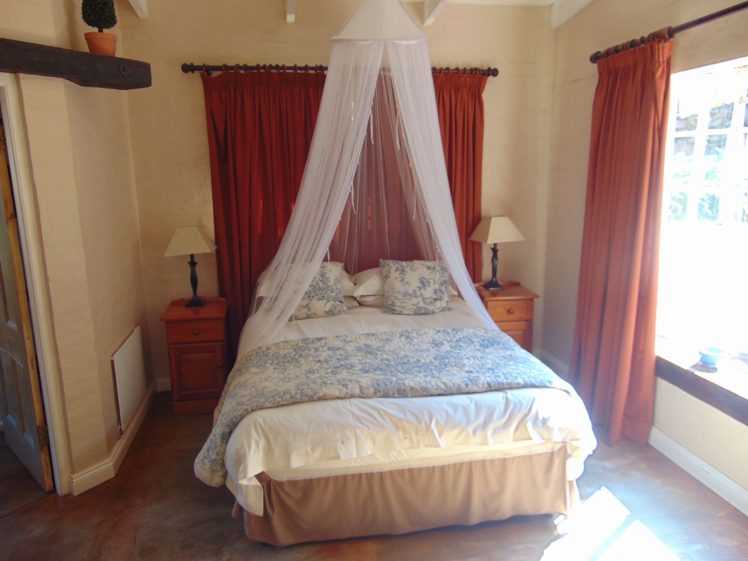 A bedroom with a four-poster bed, red curtains, and a window with a view.