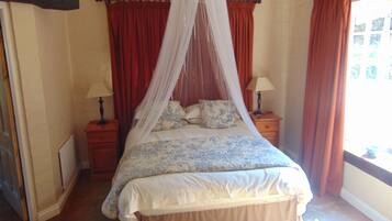 A bedroom with a four-poster bed, red curtains, and a window with a view.