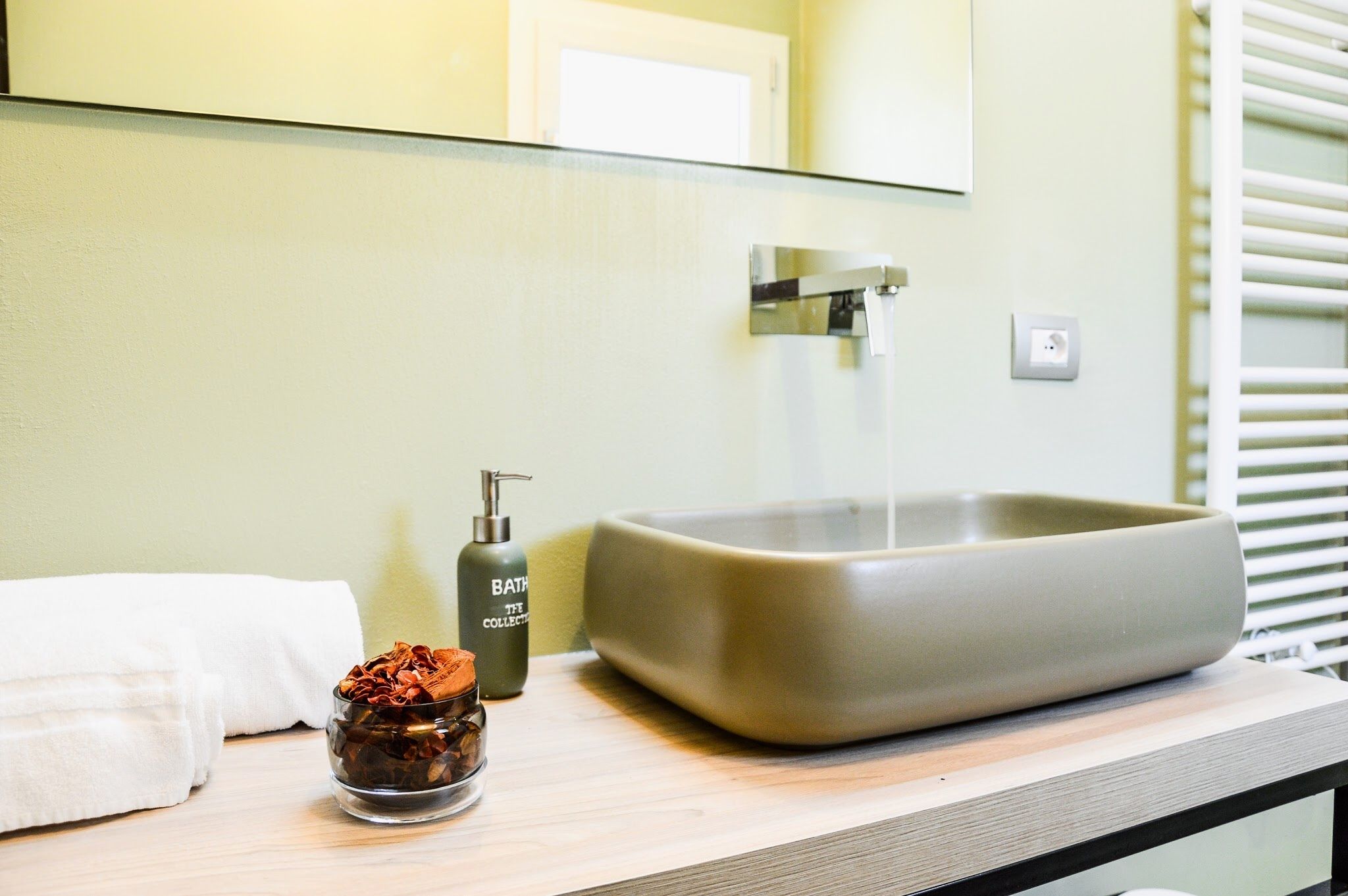A bathroom with a large rectangular sink, a towel, and a small glass jar with a pump bottle.