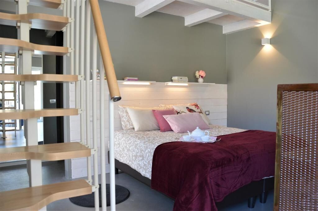 Un dormitorio con cama, una escalera de madera, una mesita de noche y una lámpara fijada a la pared.